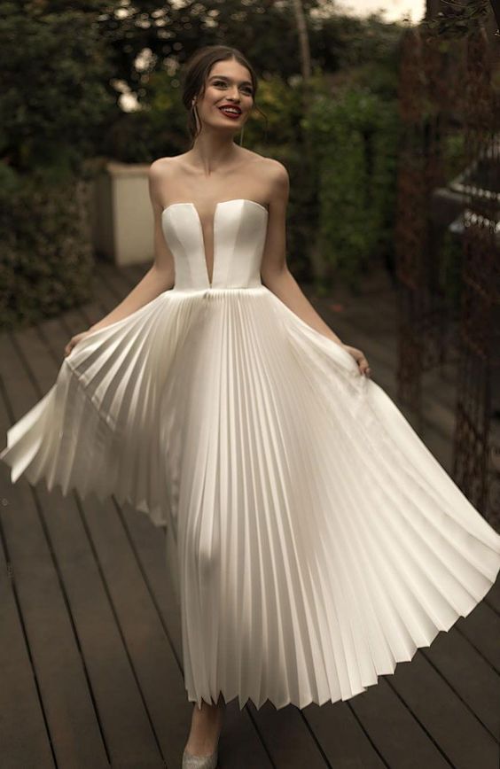 an exquisite A line wedding dress with a corset bodice with a plunging neckline and a pleated midi skirt is an out of the box idea