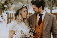boho winter wedding looks – a boho lace sheath wedding dress plus a hat and a plaid blazer, an orange waistcoat and a brown tie