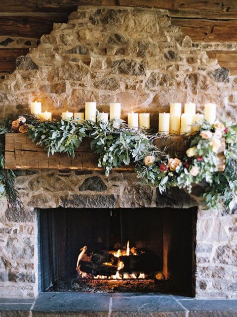 pillar candles on the mantel and lush greenery and blooms make the rough stone fireplace softer