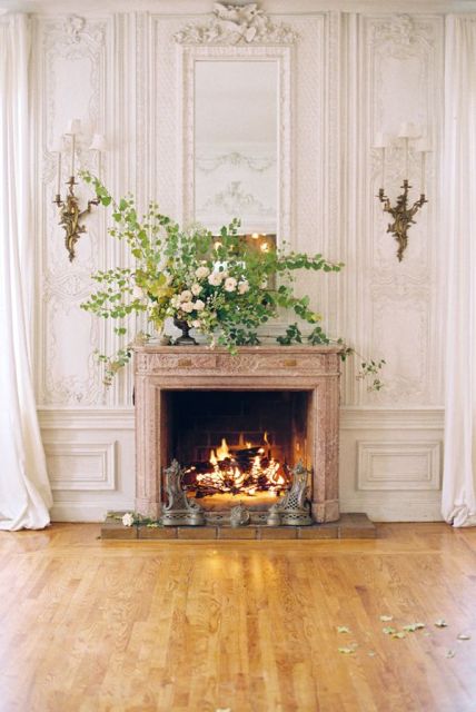 a working fireplace with a lush greenery and floral arrangement in the vase on the mantel looks very elegant