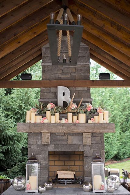 large candles, pink blooms, greenery, antlers, candle lanterns style the rough stone fireplace and make it chic