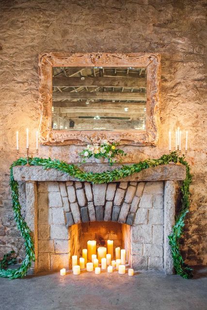 pillar candles in the fireplace, a lush greenery garland and a pastel bloom and greenery arrangement on the mantel
