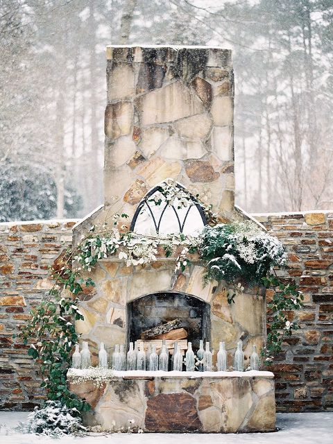 a frozen fireplace with firewood, greenery and bottles that can be used as candleholders