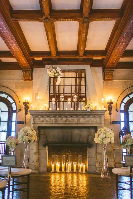 a fireplace styled with candles inside and on the mantel and neutral floral arrangements in bottles and vases