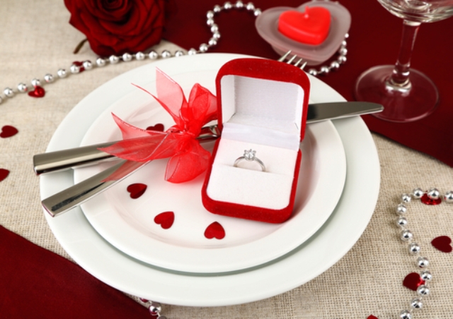 a pretty burgundy, red and white Valentine engagement table with a white runner and plates, with little red hearts, pearls and an engagement ring