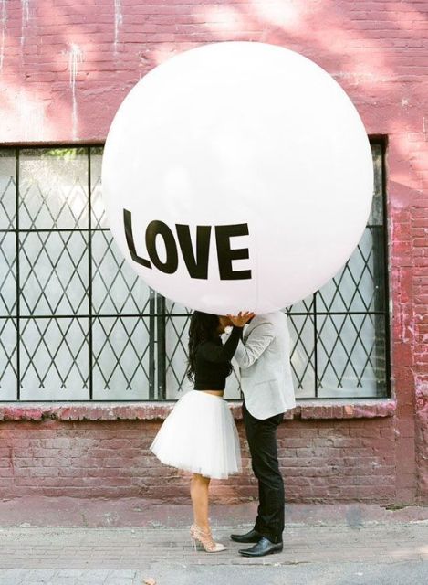 a romantic Valentine's Day engagement pic with an oversized white balloon and a couple wearing a monochromatic outfit