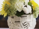 a newspaper vase with white and yellow blooms and greenery is a cool and fresh idea of a centerpiece for any wedding