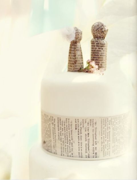 a white wedding cake covered with newspaper and with newspaper cake toppers shaped as dolls is a very nice idea with a fresh feel
