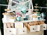 a white shabby chic vintage dresser as a wedding dessert table with a banner and lots of various candies, sweets and desserts