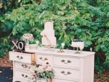 a white vintage dresser decorated with blooms and greenery and a chalkboard sign and used as a wedding cake table with cakes and other sweets is a great idea for a vintage wedding
