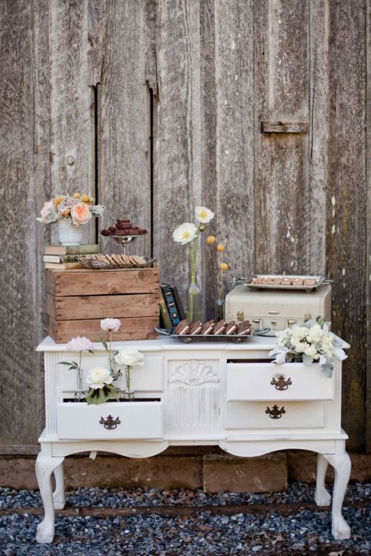 a white vintage dresser as a wedding dessert table with neutral and pastel blooms and various sweets all over the table