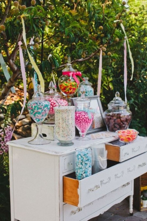 a white vintage dresser as a wedding sweets table, with various colorful sweets and candies and bright ribbon over the table