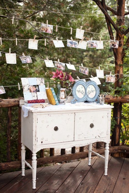 a white vintage dresser used for wedding decor with signs, books, couple's photos and banners of photos over the dresser