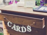 a stained vintage dresser with a banner used for storing wedding cards and wishes is a cool and smart solution for a rustic wedding