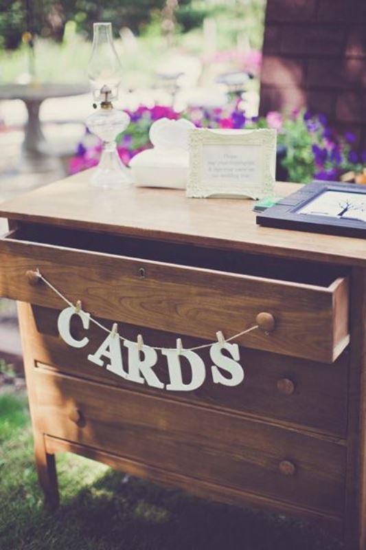a stained vintage dresser with a banner used for storing wedding cards and wishes is a cool and smart solution for a rustic wedding