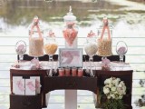 a vintage dark-stained dresser used as a wedding dessert table with candies and sweets and a floral arrangement, with blooms hanging over it