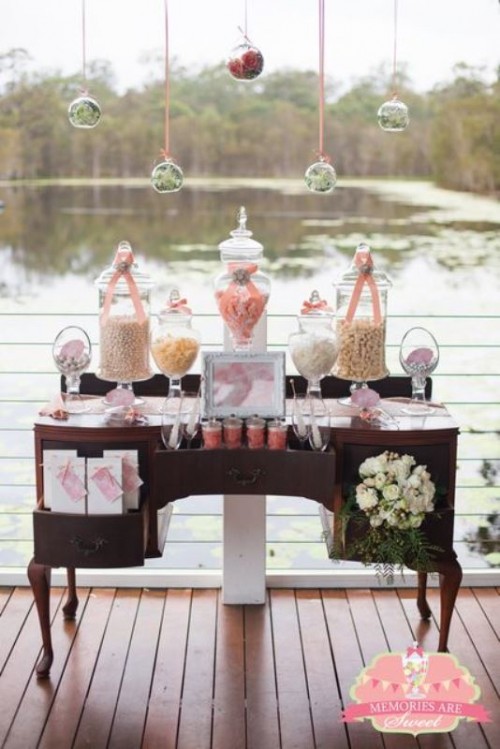 a vintage dark-stained dresser used as a wedding dessert table with candies and sweets and a floral arrangement, with blooms hanging over it