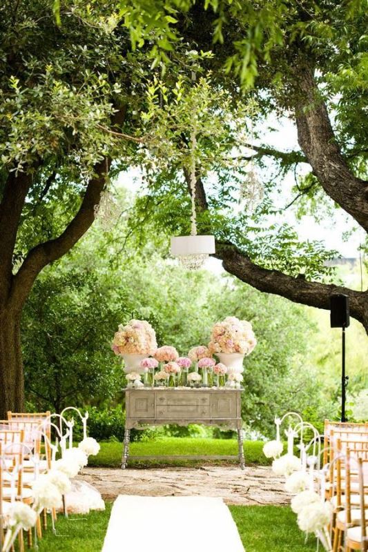 a rustic vintage wedding altar of a greyish dresser with lots of pastel blooms in various vases and planters plus matching floral arrangements on the chairs
