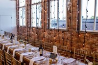an industrial wedding venue with brick walls, hanging lights, a rose gold sequin tablecloth and candles plus neutral blooms