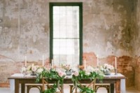 an industrial wedding venue with shabby chic walls and brick walls and a very refined wedding tablescape with candles, greenery and pink blooms
