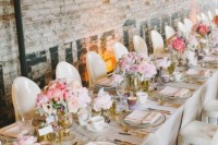 an industrial wedding venue with letters on the walls, a long table accented with pink blooms, gold edge pieces and gold cutlery
