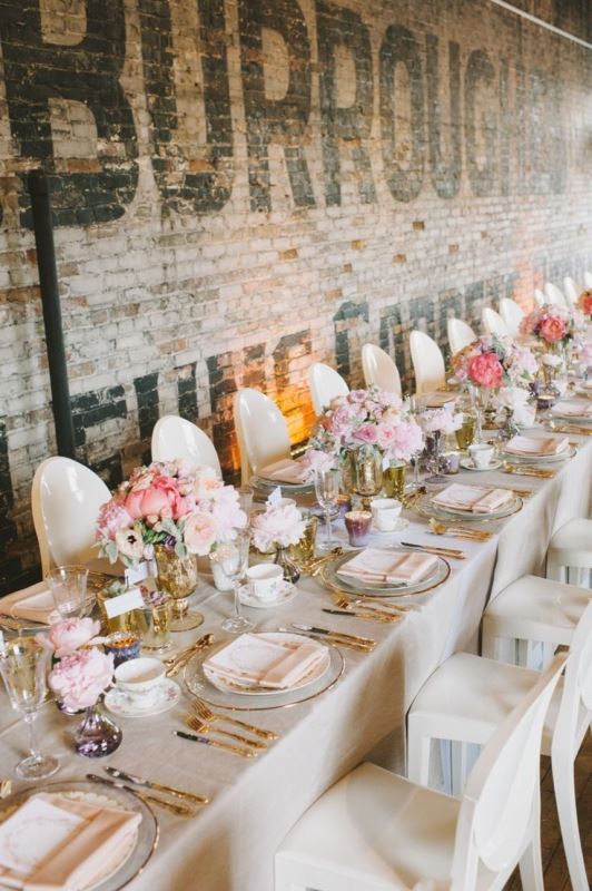 an industrial wedding venue with letters on the walls, a long table accented with pink blooms, gold edge pieces and gold cutlery