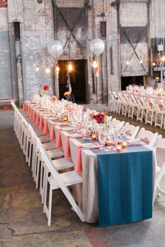 an industrial wedding venue with grey brick walls, pendant bulbs and bright wedding tablescapes in blue and coral
