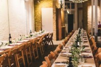 an industrial wedding venue with brick walls, lights hanging over the space, greenery table runners and candles