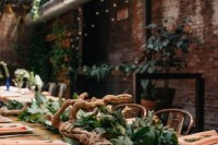 an industrial wedding venue with brick walls, exposed pipes, lights and greenery runners and driftwood is lit up with skylights