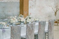 a shabby chic industrial wedding venue with brick walls, pillars and a lovely decorated table with neutral blooms, silver sequin covered chairs and a chandelier