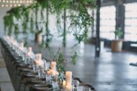 an industrial wedding venue with exposed pipes and brick walls, lights and rough wooden tables is softened with hanging greenery and candles on the table