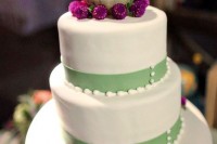 a white wedding cake with a green ribbon and a globe topper plus some blooms for a bright touch