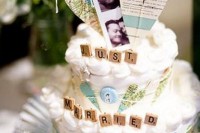 a white wedding cake with hearts cut out of a world map and some scrabble letters for decor
