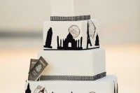 a stylish white and black wedding cake with London views and famous sights and fresh white blooms on top