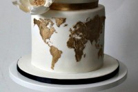 a white wedding cake with gold stripes and a gold world map plus an oversized sugar bloom