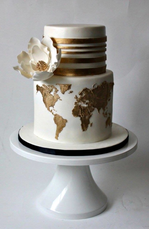 a white wedding cake with gold stripes and a gold world map plus an oversized sugar bloom