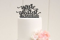 a chic white wedding cake with sugar blooms and a black calligraphy topper telling of adventures and travelling