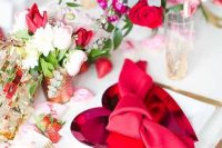 a beautiful Valentine engagement tablescape with pink heart chargers, gold cutlery, bold blooms and greenery