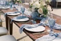 a beautiful wedding tablescape with serenity blue glasses and napkins, neutral blooms and greenery and gold cutlery