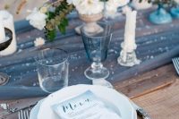 a blue beach reception table with a sheer blue runner, some sparkles, a white and blue floral centerpiece and ombre blue menus