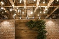 a boho wedding ceremony space with a wooden backdrop with lush textural greenery, pillar candles and chairs