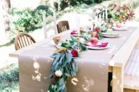 a bold fall wedding tablescape with a kraft paper table runner, a greenery and floral one, burgundy napkins, apples and tall and thin candles