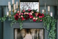 a bold modern fireplace with lots of candles inside and on the mantel, with an antique mirror and a lush floral and greenery garland
