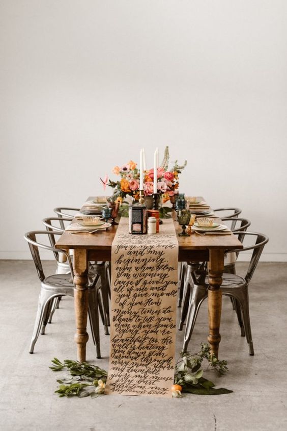 a bold wedding tablescape with a kraft paper calligraphy table runner, bold blooms and greenery, tall and thin candles and metal chairs