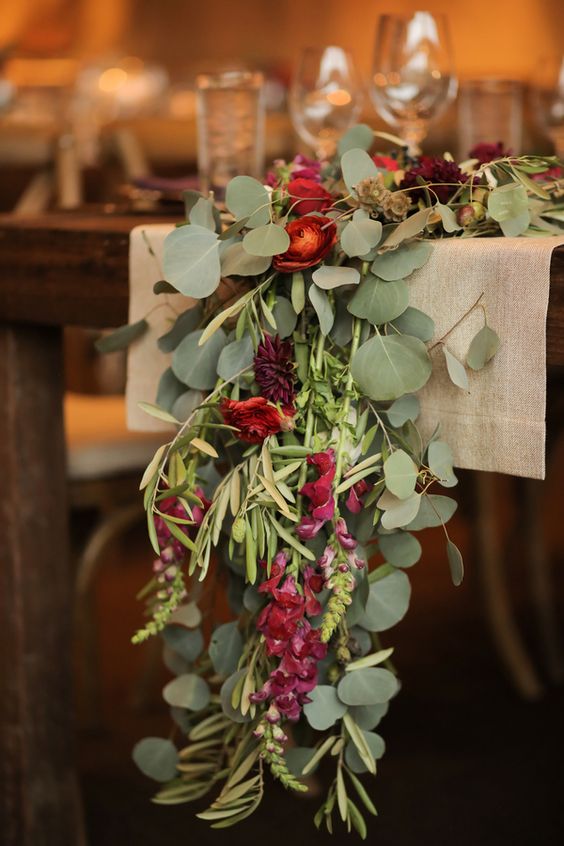 a burlap table runner, a greenery runner with red and burgundy blooms and candles for decorating a ski resort reception