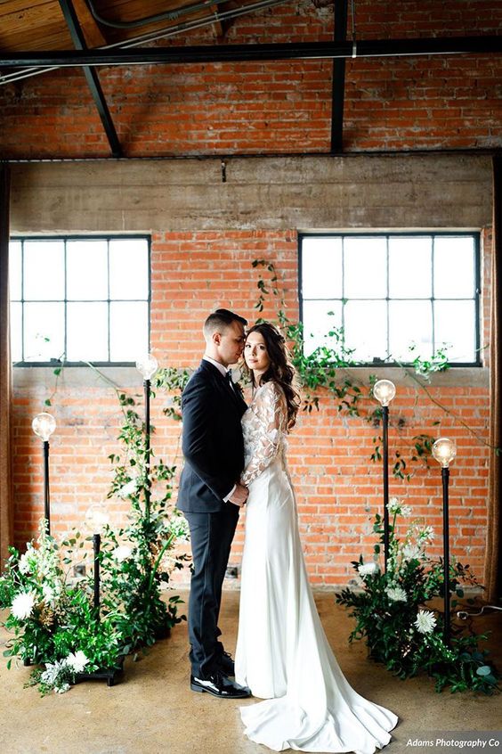 a chic industrial wedding ceremony space decorated with greenery, white blooms and catchy floor lamps