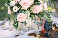 a chic pastel wedding tablescape with a serenity blue table runner and napkins, blush roses and greenery, navy glasses and gold cutlery