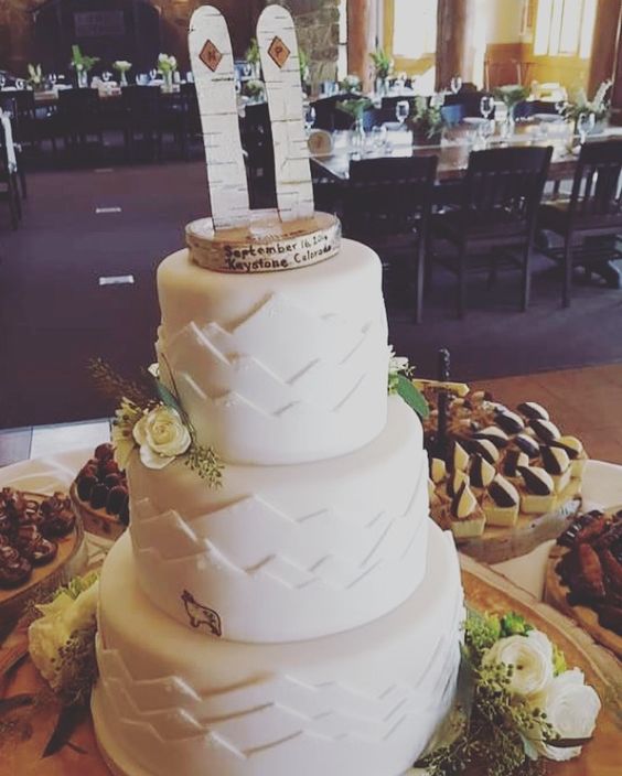 a cool white textural wedding cake with blooms and a wood slice with wooden snowboards on top for a themed wedding