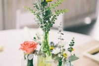 a cute and bright wedding centerpiece of yellow and green bottles, bright blooms and fresh greenery plus some candles