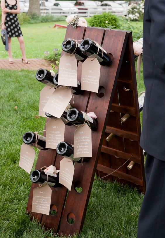 a dark stained stand with wine bottles as escort cards is a lovely idea for a rustic or a vineyeard wedding or if you just enjoy wine a lot